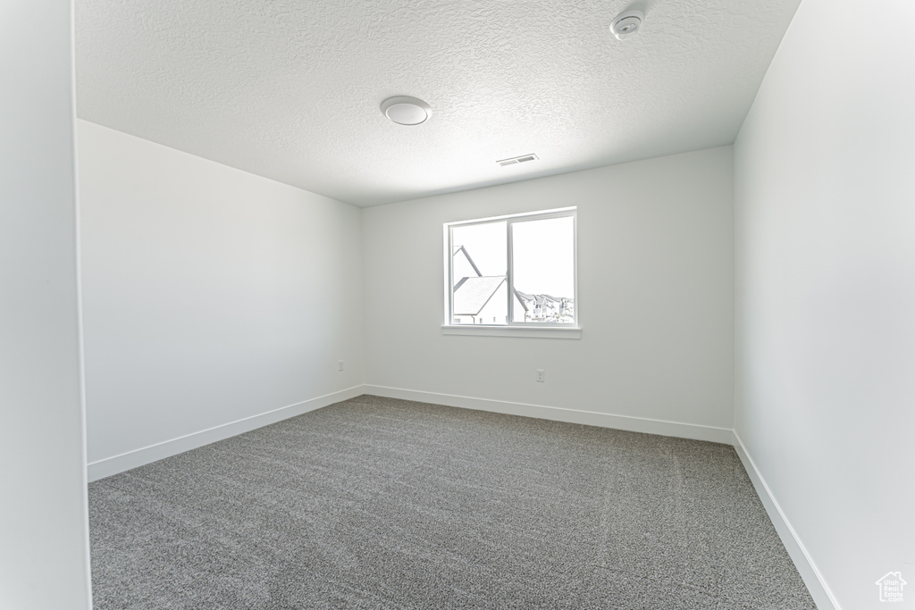 Carpeted empty room with a textured ceiling and a smoke detector