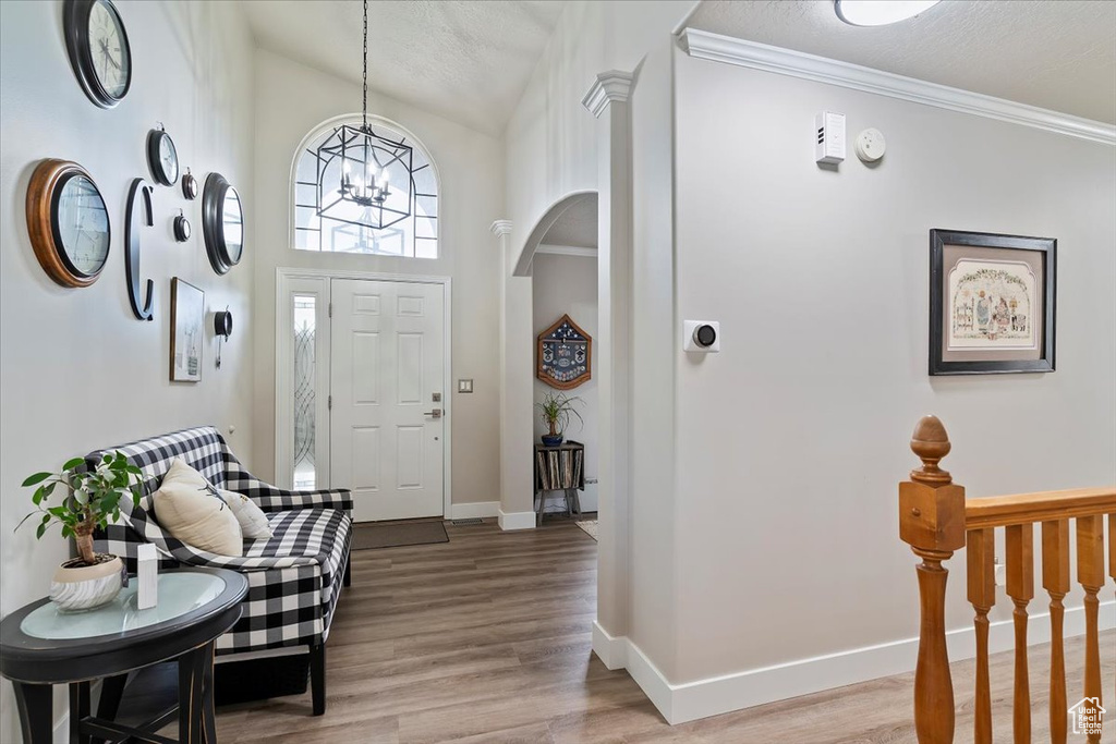 Foyer with light wood-style flooring, a textured ceiling, a chandelier, a high ceiling, and baseboards