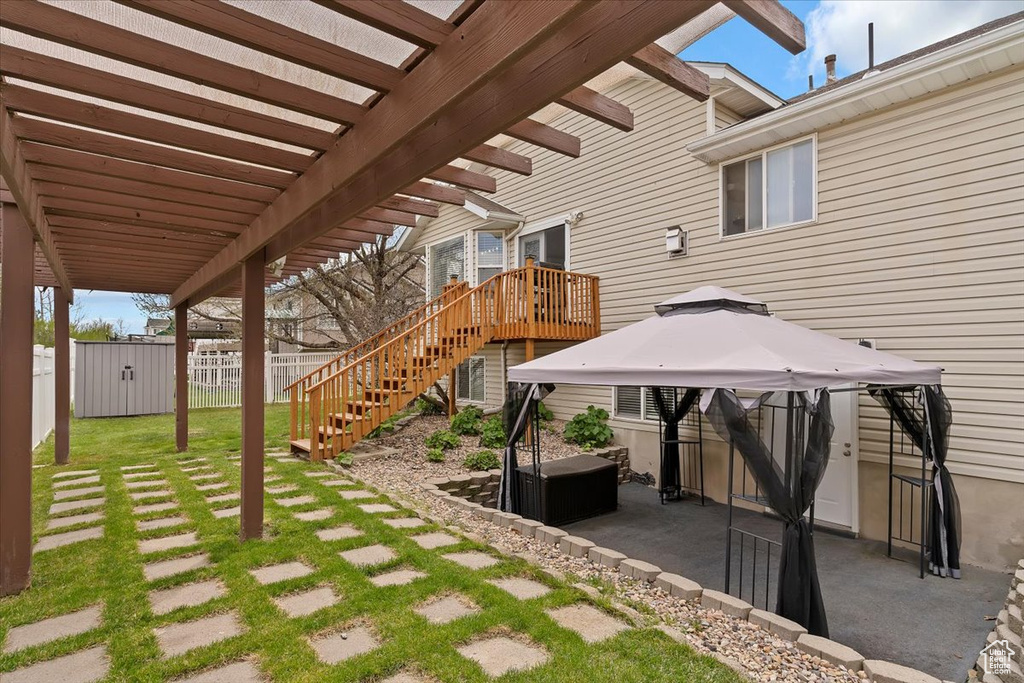 View of patio / terrace with a pergola, a gazebo, fence, an outdoor structure, and a storage unit