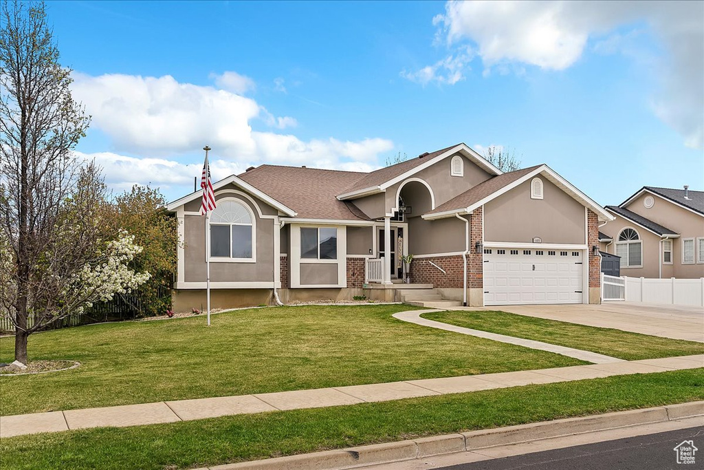 View of front of house featuring an attached garage, fence, stucco siding, a front lawn, and driveway