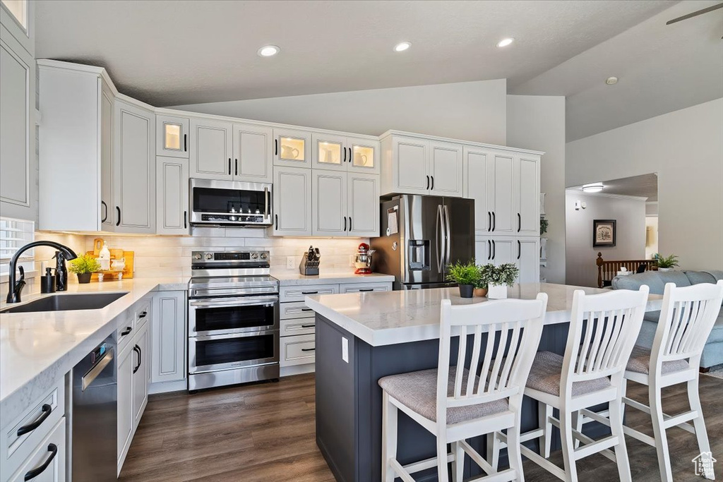 Kitchen with glass insert cabinets, appliances with stainless steel finishes, a sink, lofted ceiling, and decorative backsplash