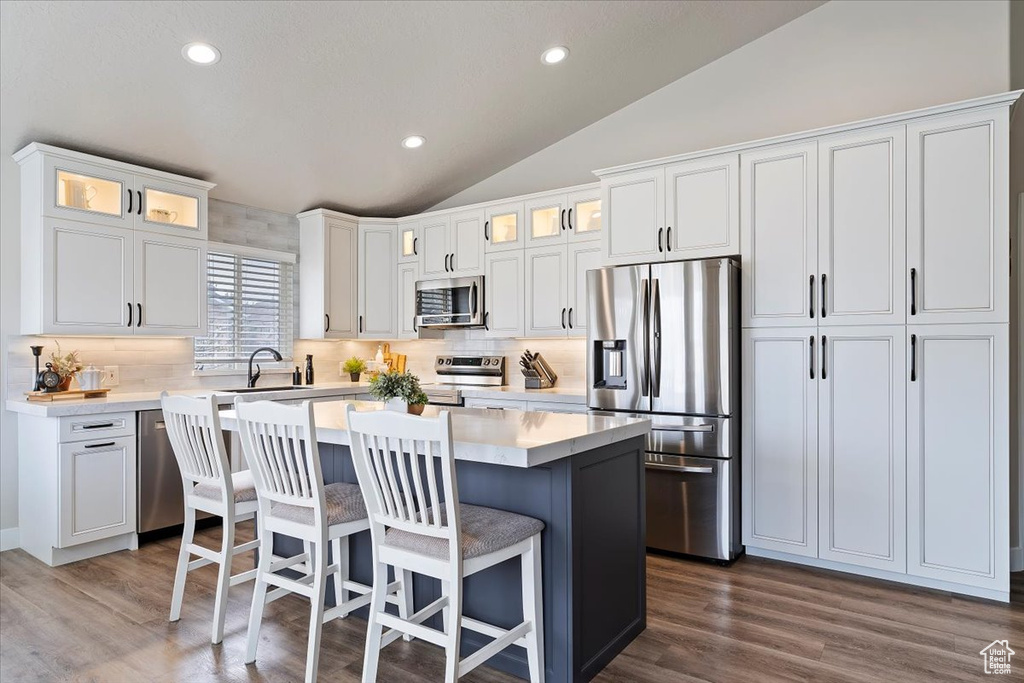 Kitchen featuring lofted ceiling, a center island, decorative backsplash, and appliances with stainless steel finishes