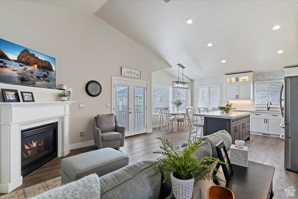 Living area featuring a glass covered fireplace, baseboards, recessed lighting, high vaulted ceiling, and wood finished floors