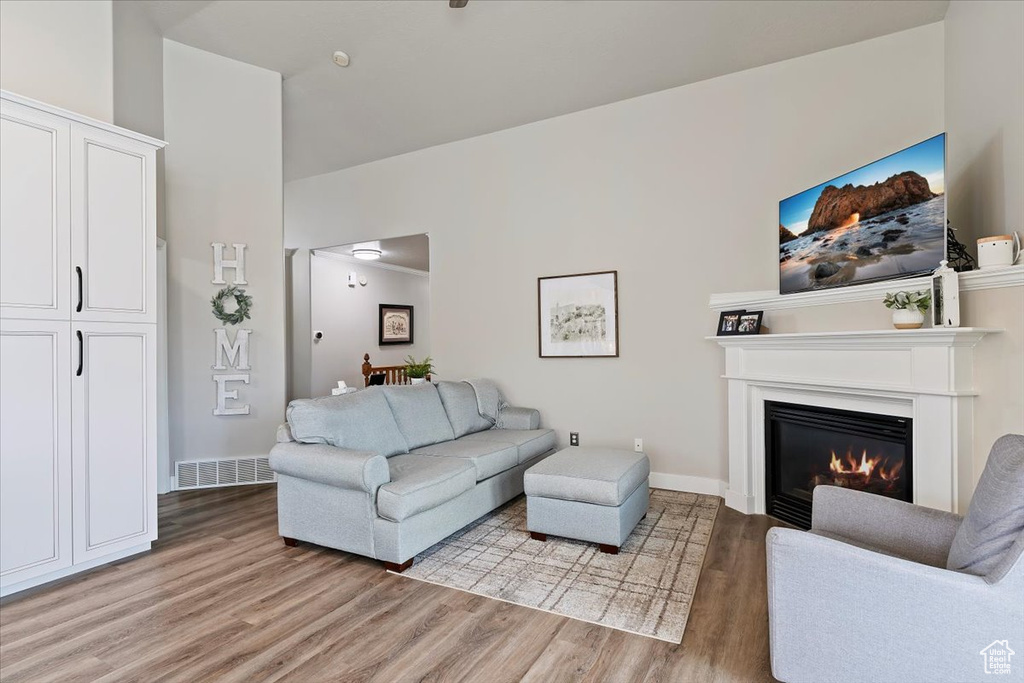 Living area featuring visible vents, light wood-style flooring, a glass covered fireplace, and baseboards