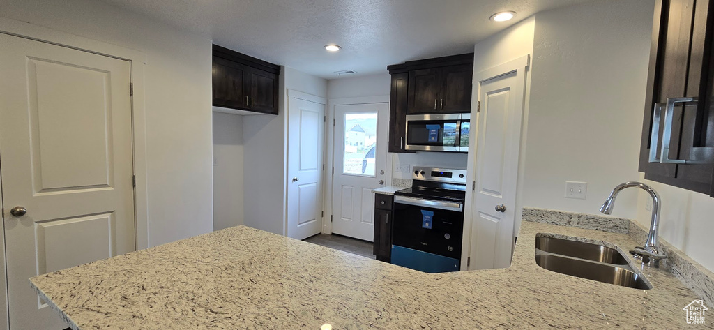 Kitchen with stainless steel appliances, a sink, light stone countertops, recessed lighting, and a peninsula