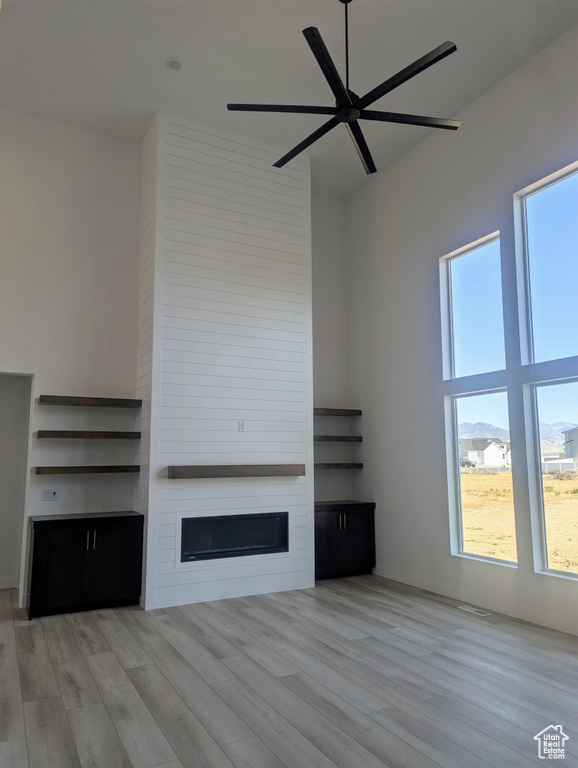 Unfurnished living room with wood finished floors, a large fireplace, a ceiling fan, and a high ceiling
