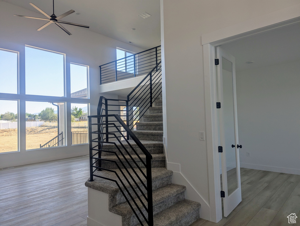 Stairway featuring wood finished floors, a ceiling fan, and a high ceiling