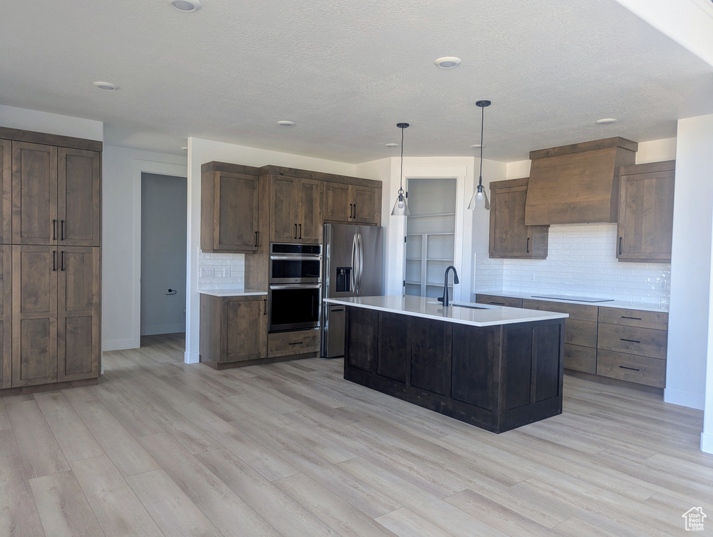 Kitchen featuring custom exhaust hood, stainless steel appliances, backsplash, light countertops, and light wood-style floors
