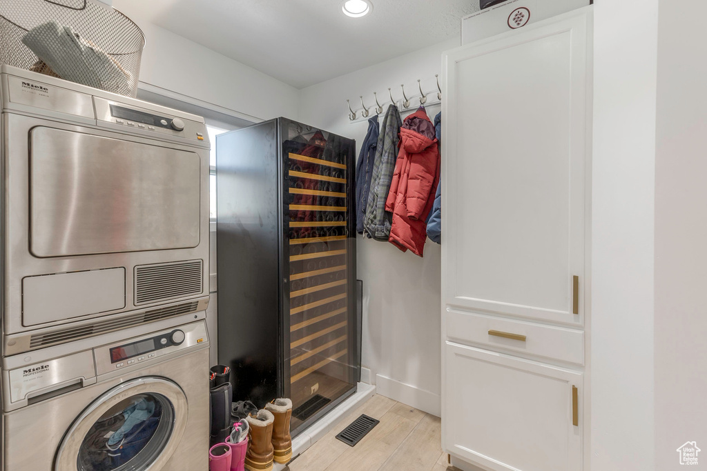 Laundry area with stacked washer / drying machine, light wood finished floors, recessed lighting, and beverage cooler