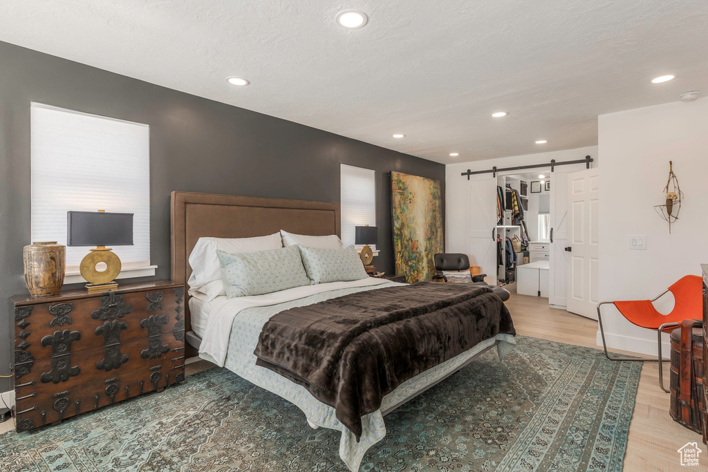 Bedroom with a barn door, light wood-style flooring, recessed lighting, a spacious closet, and a closet