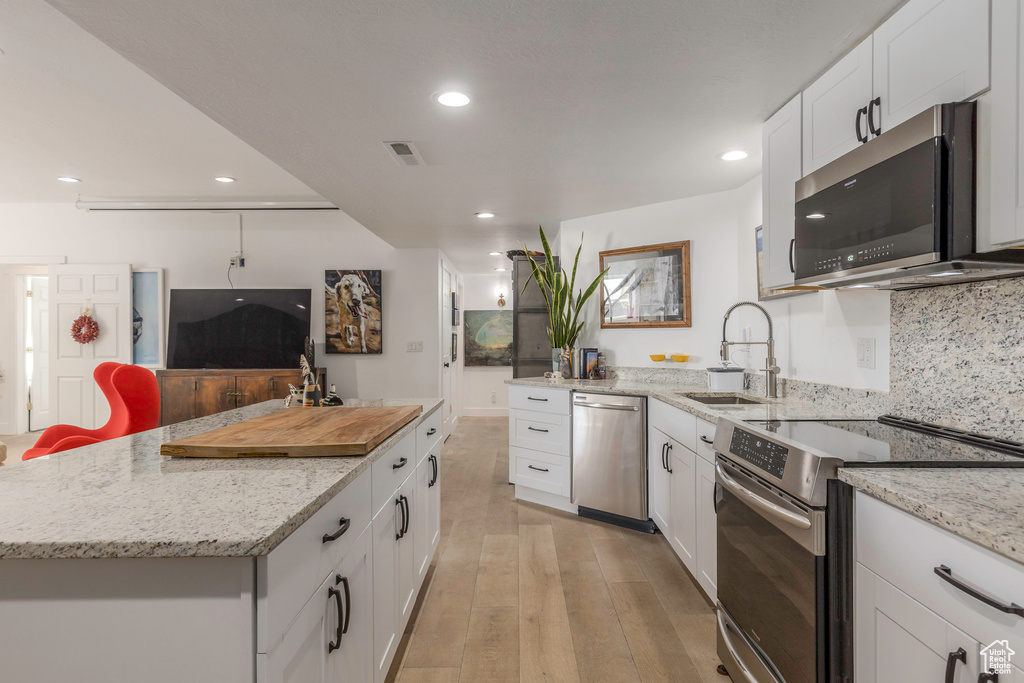 Kitchen featuring appliances with stainless steel finishes, a sink, recessed lighting, light wood-style flooring, and white cabinets