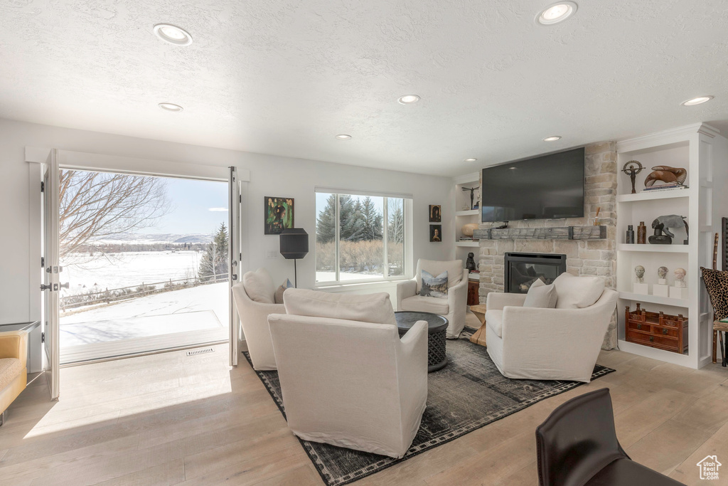 Living room featuring recessed lighting, a stone fireplace, light wood-style floors, a textured ceiling, and built in shelves