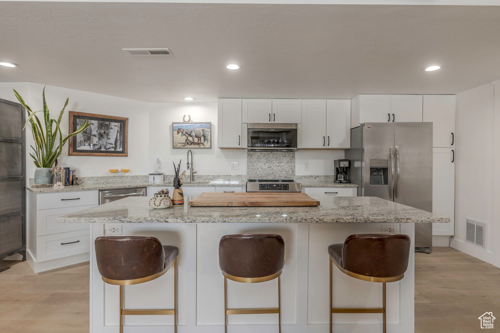 Kitchen featuring stainless steel appliances, a breakfast bar area, white cabinetry, a kitchen island, and recessed lighting