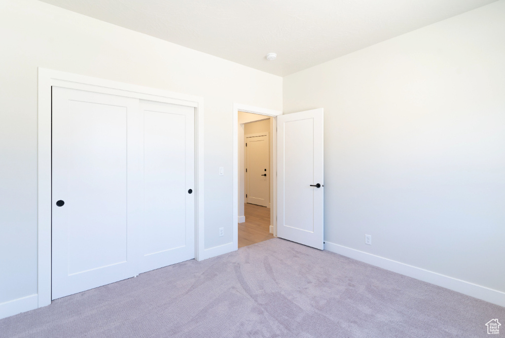 Unfurnished bedroom featuring light carpet, a closet, and baseboards
