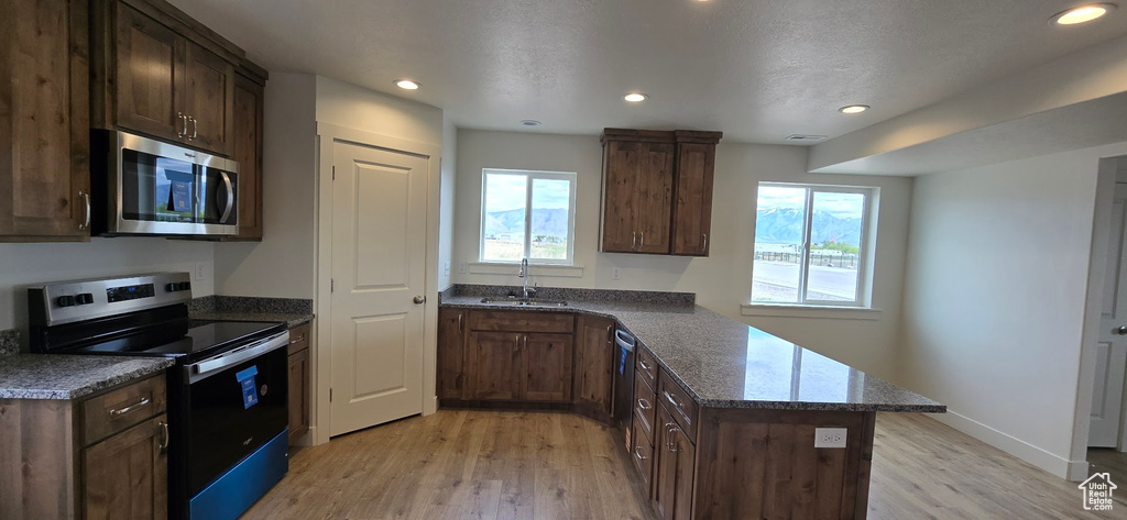 Kitchen featuring stainless steel appliances, a sink, light wood-style floors, a peninsula, and dark stone countertops