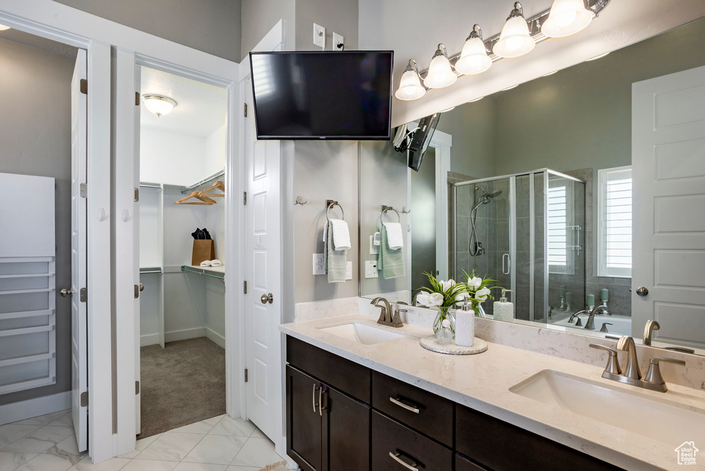 Full bath featuring a sink, a walk in closet, a shower stall, and double vanity