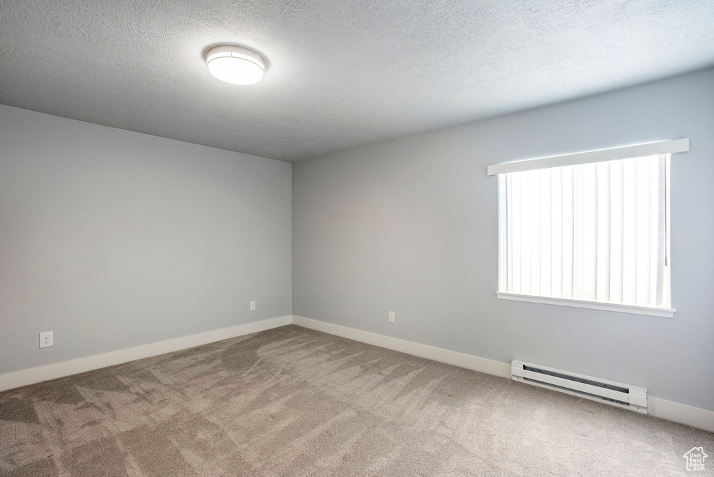 Carpeted spare room with baseboard heating, a textured ceiling, and a healthy amount of sunlight