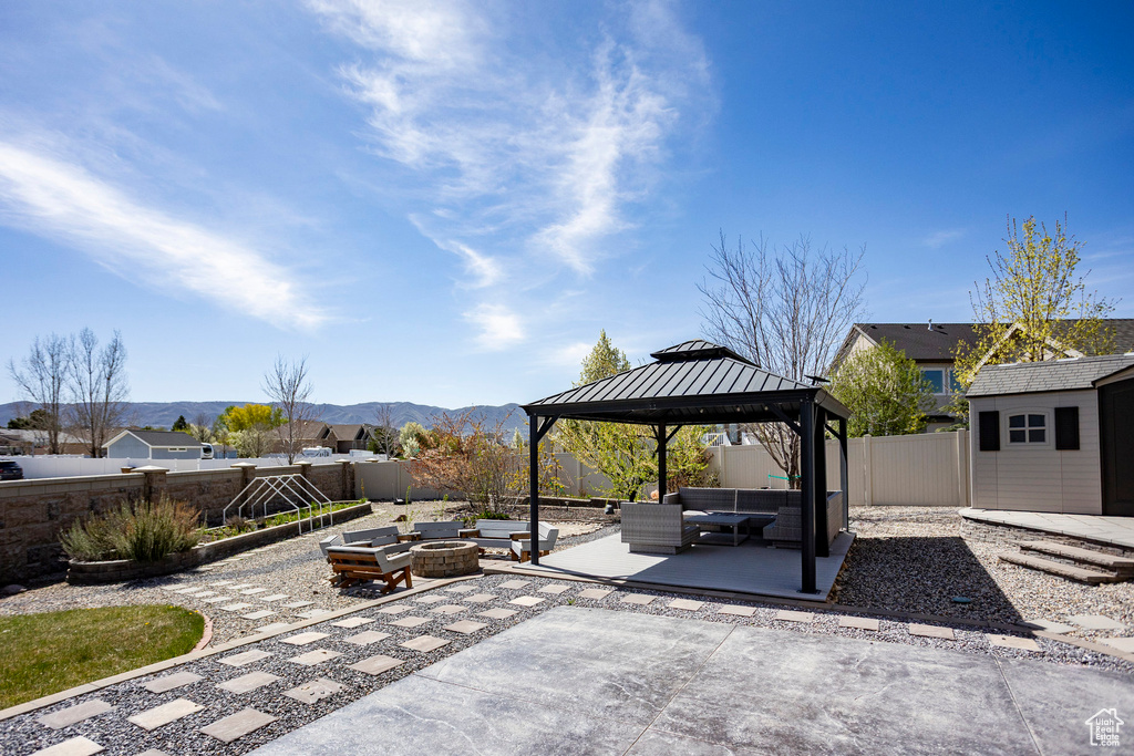 View of patio with a mountain view, an outdoor living space with a fire pit, an outbuilding, a gazebo, and a storage unit