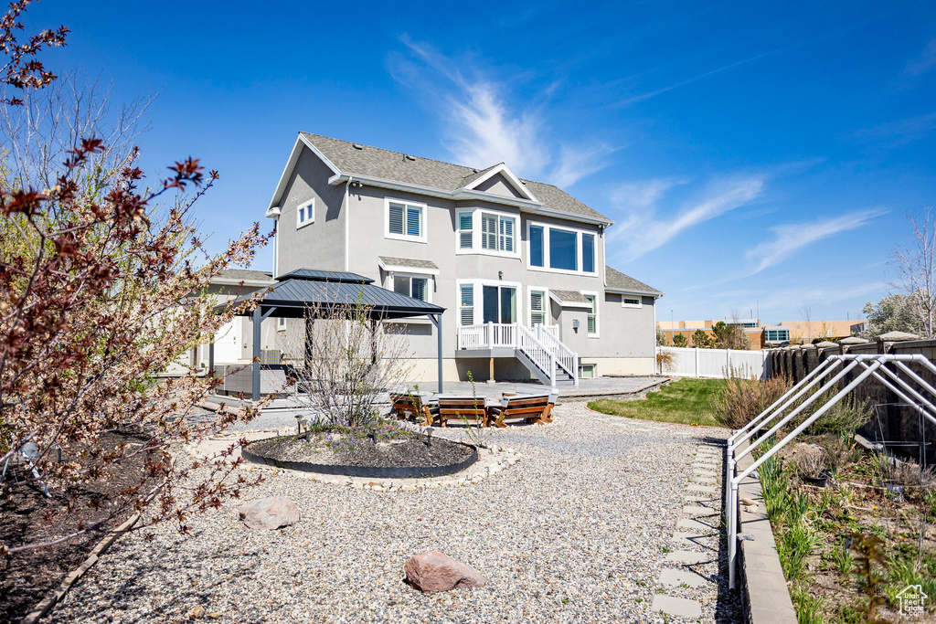 Back of property with a shingled roof, a patio area, a gazebo, fence, and stucco siding