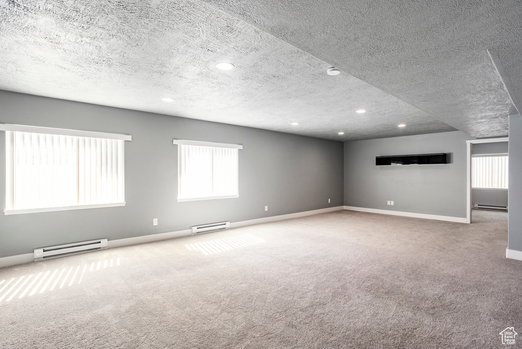 Carpeted spare room featuring baseboards, a baseboard heating unit, and a textured ceiling