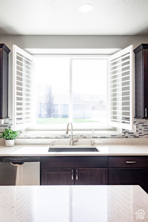 Kitchen with dishwasher, a sink, dark brown cabinets, and decorative backsplash