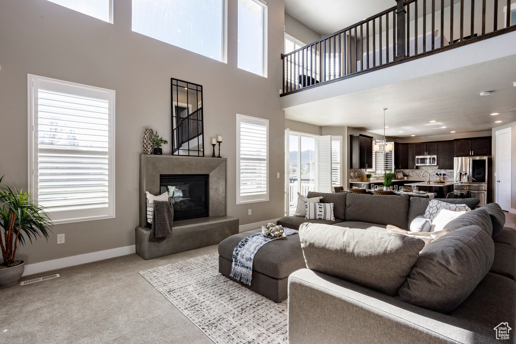 Living area featuring light colored carpet, a towering ceiling, visible vents, a premium fireplace, and baseboards