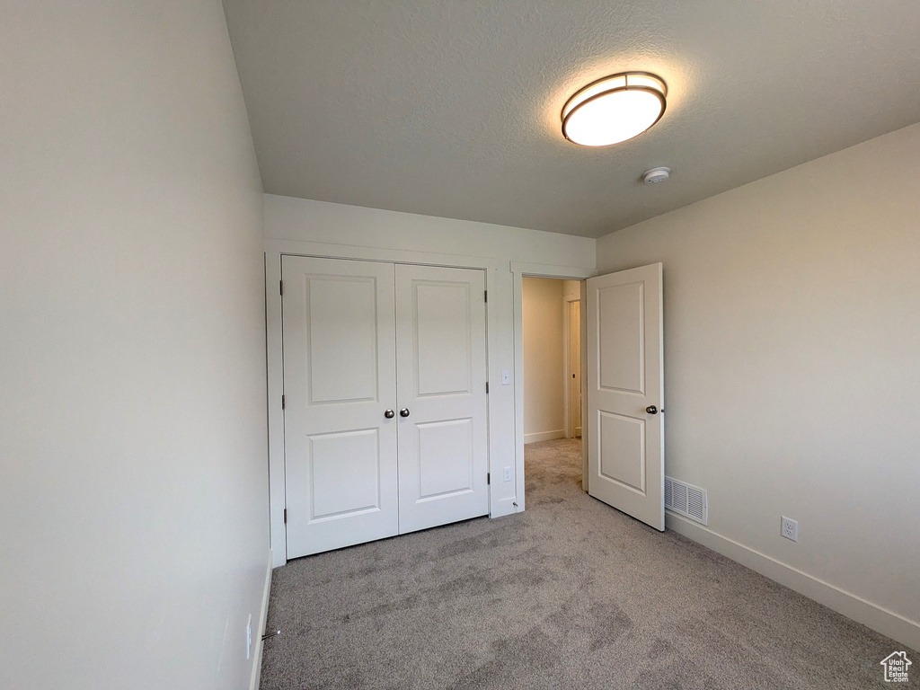 Unfurnished bedroom with a closet, baseboards, carpet flooring, a textured ceiling, and visible vents