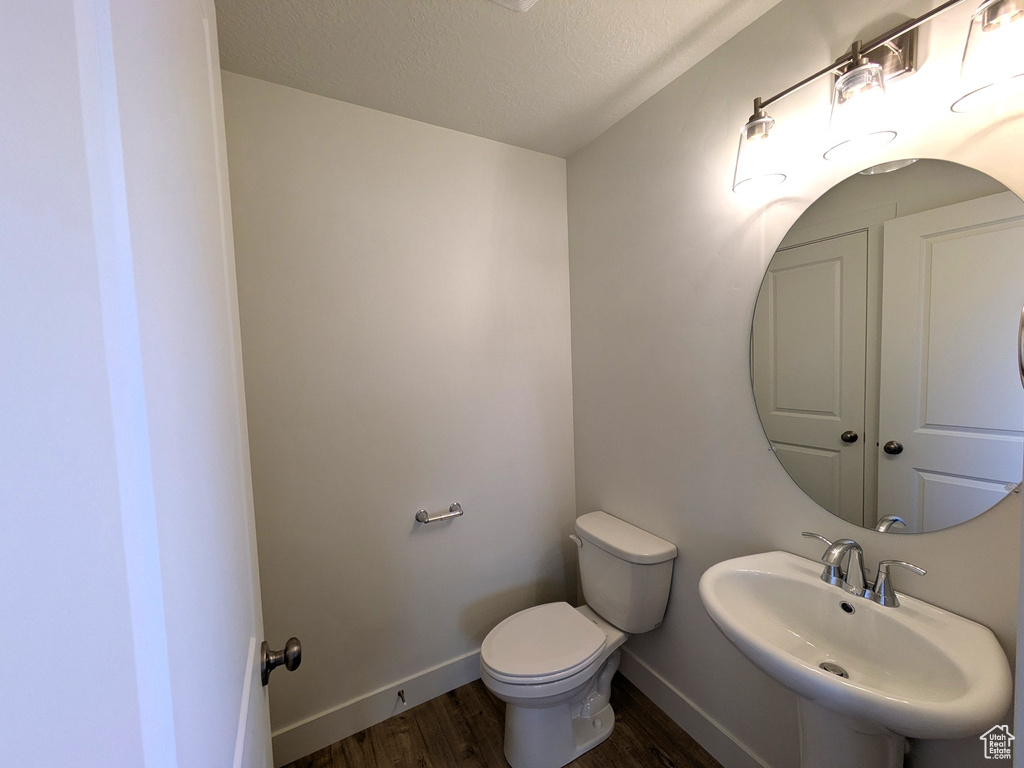 Half bath featuring a textured ceiling, toilet, wood finished floors, a sink, and baseboards