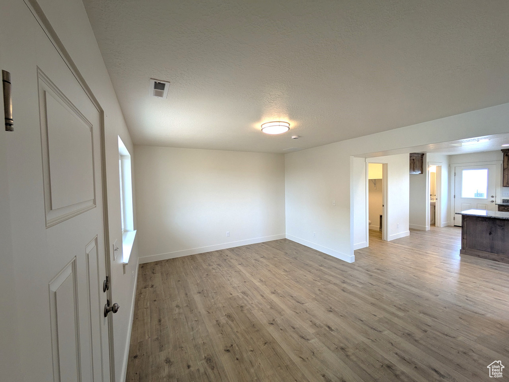 Empty room with baseboards, light wood-style flooring, a textured ceiling, and visible vents