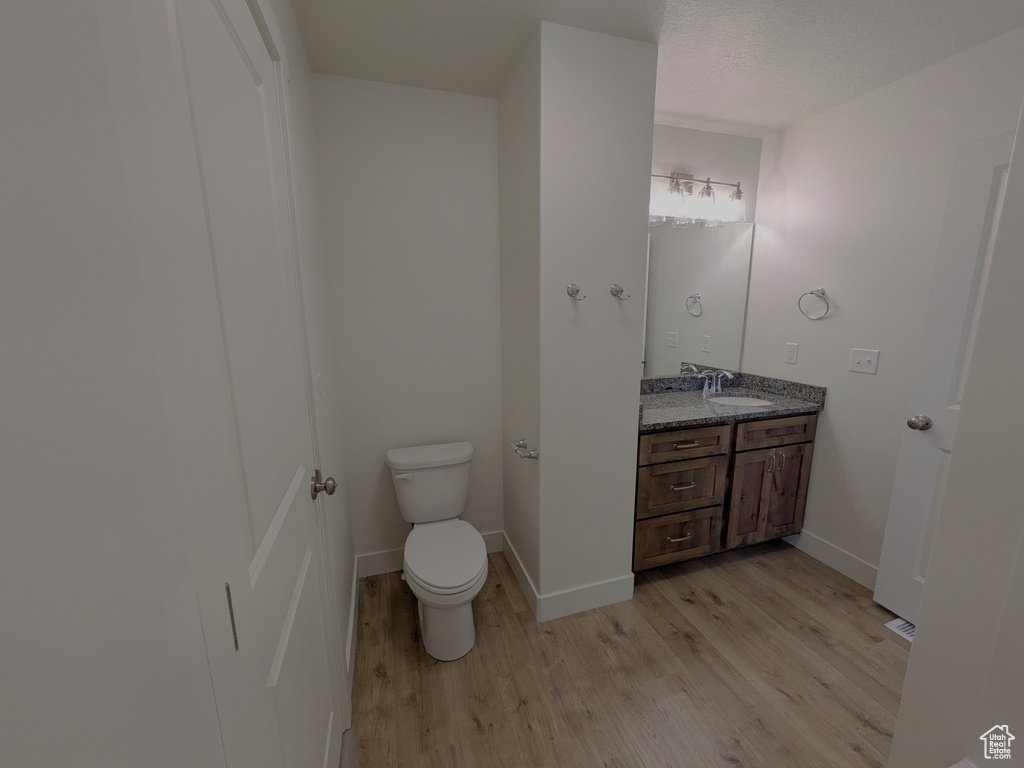 Bathroom with toilet, vanity, wood finished floors, and baseboards