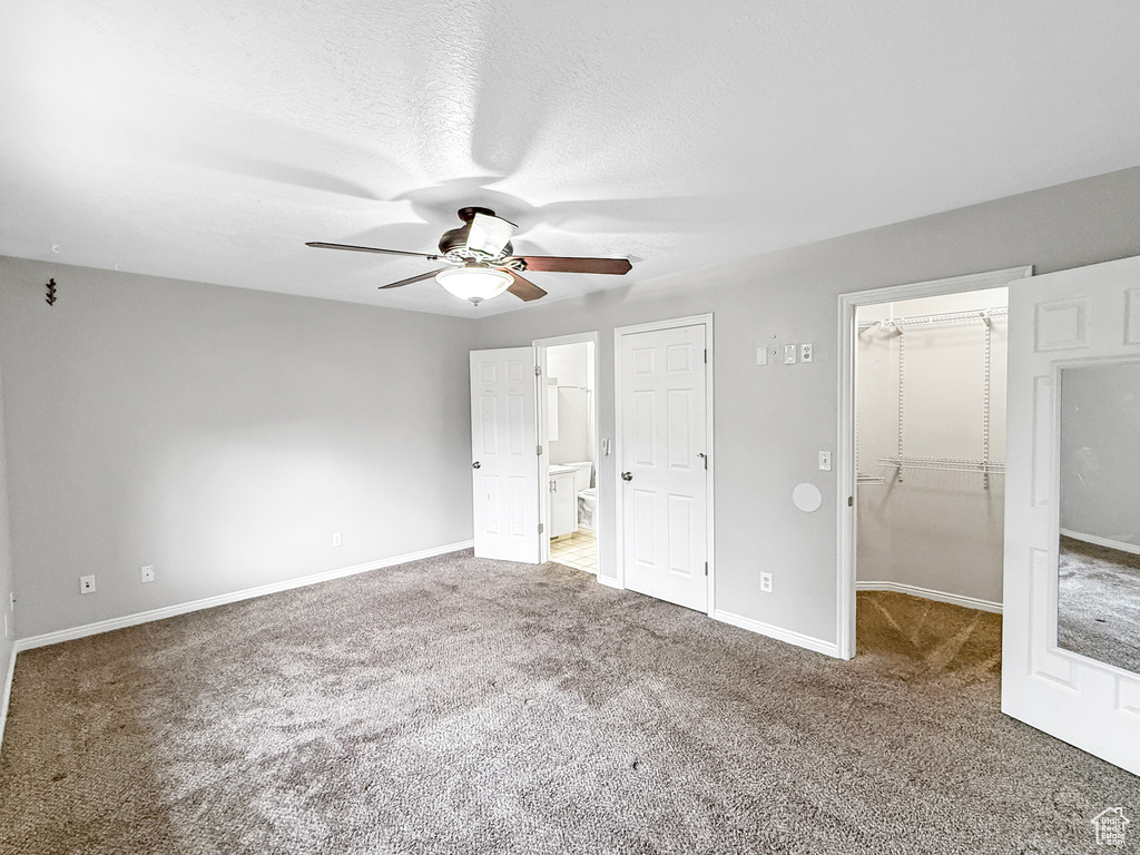 Unfurnished bedroom featuring ceiling fan, baseboards, a walk in closet, and carpet floors