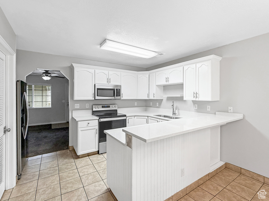 Kitchen with a peninsula, light tile patterned floors, a ceiling fan, stainless steel appliances, and a sink