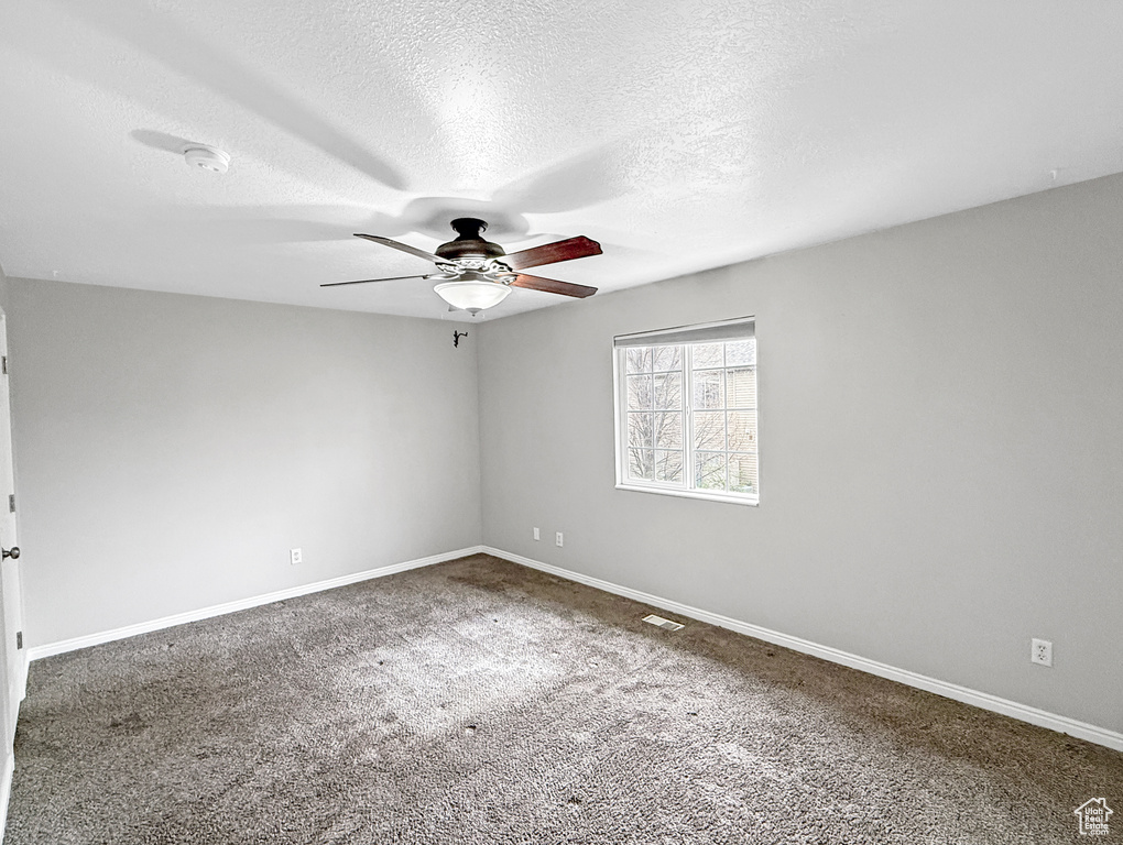 Carpeted empty room featuring baseboards, a textured ceiling, and ceiling fan