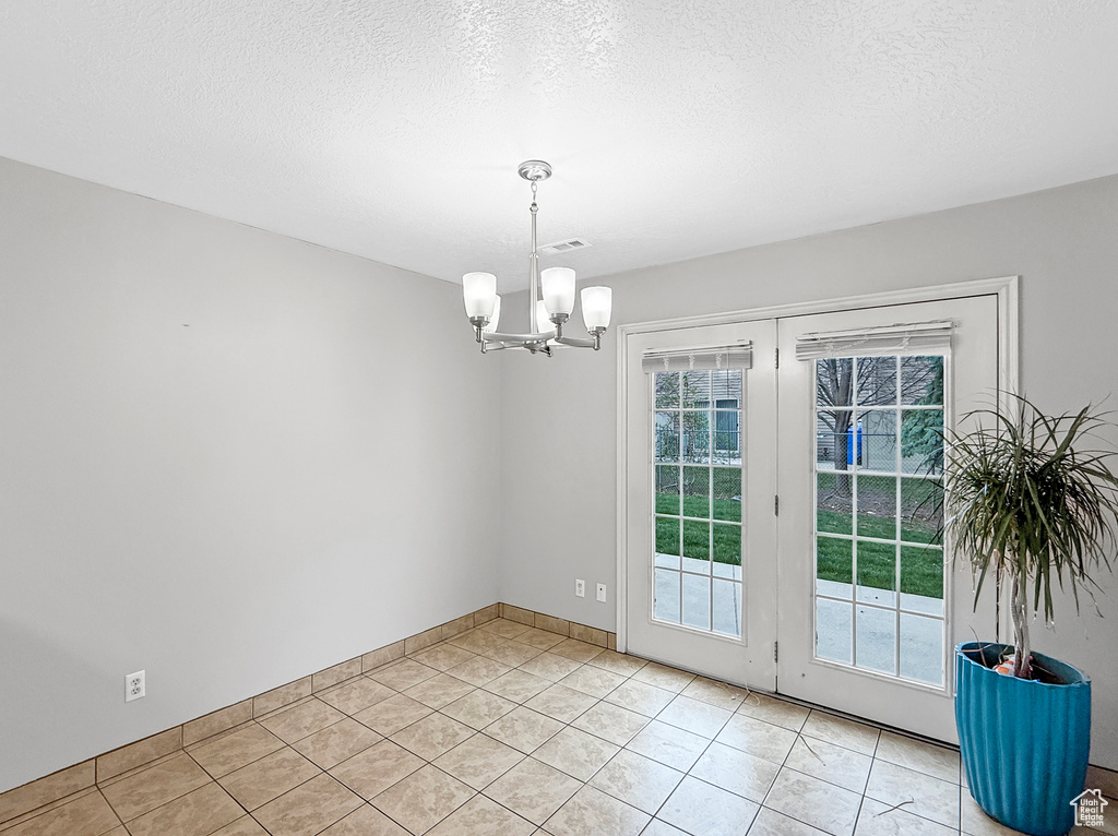 Unfurnished dining area featuring a textured ceiling, light tile patterned floors, a notable chandelier, and visible vents