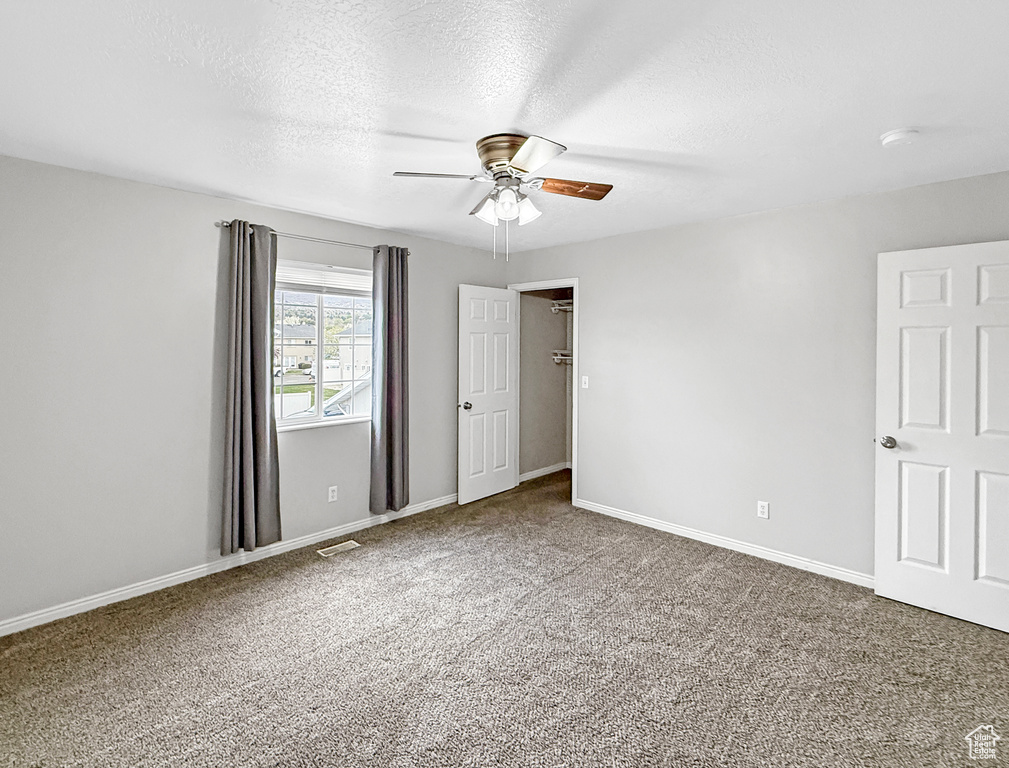 Empty room featuring visible vents, baseboards, ceiling fan, carpet, and a textured ceiling