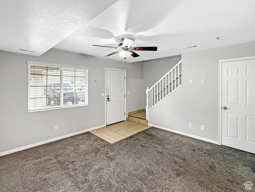 Tiled foyer entrance with baseboards, stairs, visible vents, ceiling fan, and carpet