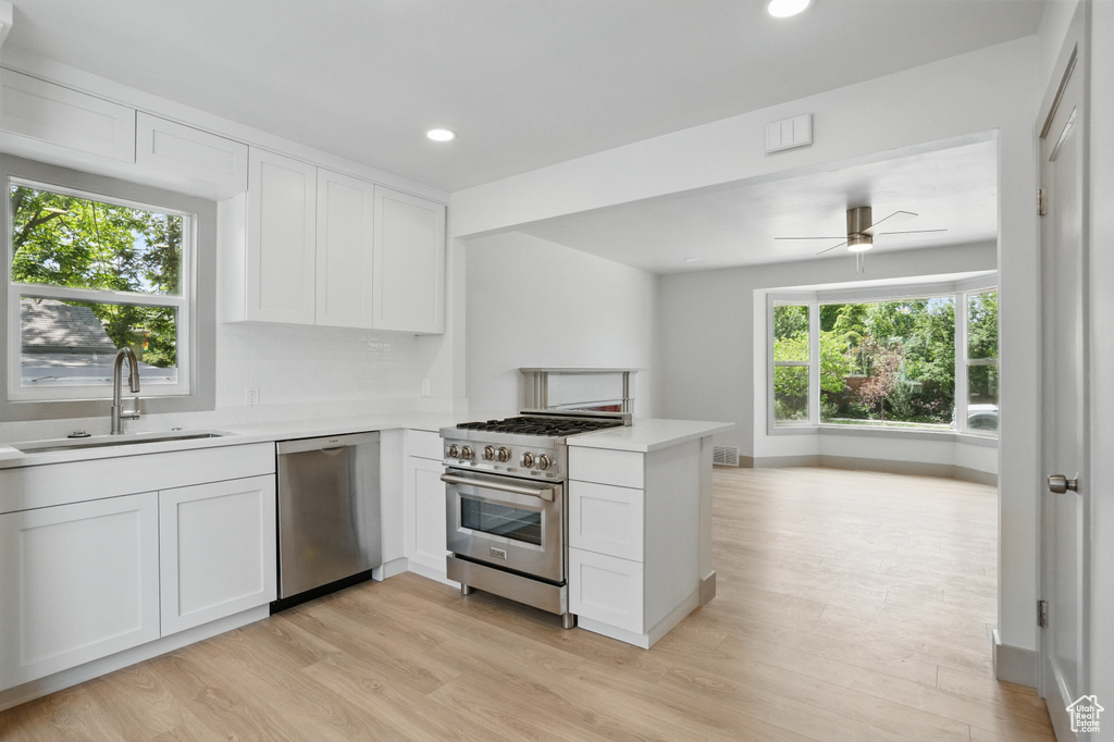 Kitchen with stainless steel appliances, a sink, light countertops, light wood-type flooring, and white cabinets