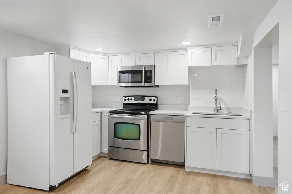Kitchen featuring stainless steel appliances, a sink, light wood-style floors, white cabinets, and light countertops