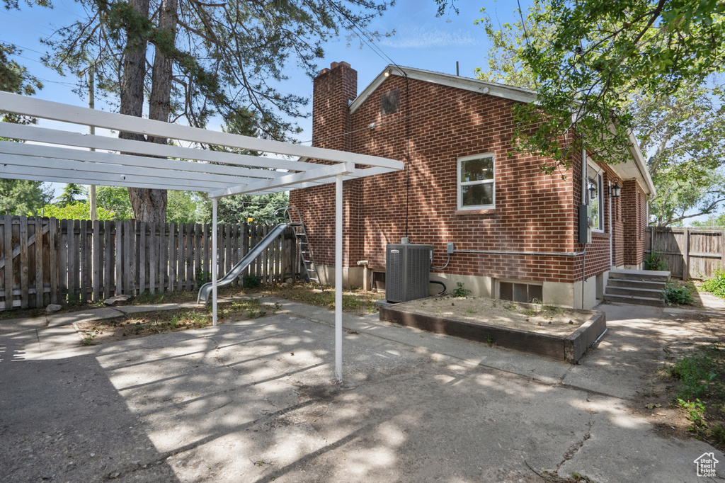 Back of property featuring central air condition unit, a chimney, a pergola, brick siding, and a patio area