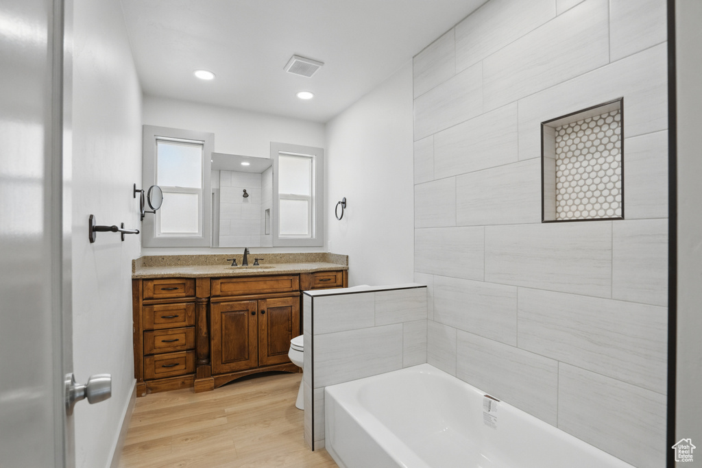 Bathroom with toilet, wood finished floors, a bath, vanity, and a shower