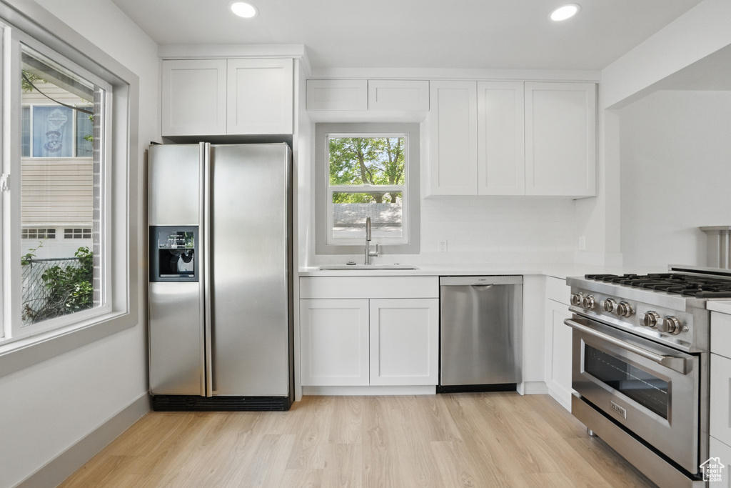 Kitchen featuring appliances with stainless steel finishes, a sink, light wood-style flooring, white cabinets, and light countertops