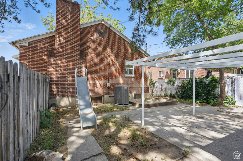 Back of house featuring central AC unit, a chimney, brick siding, and a patio area