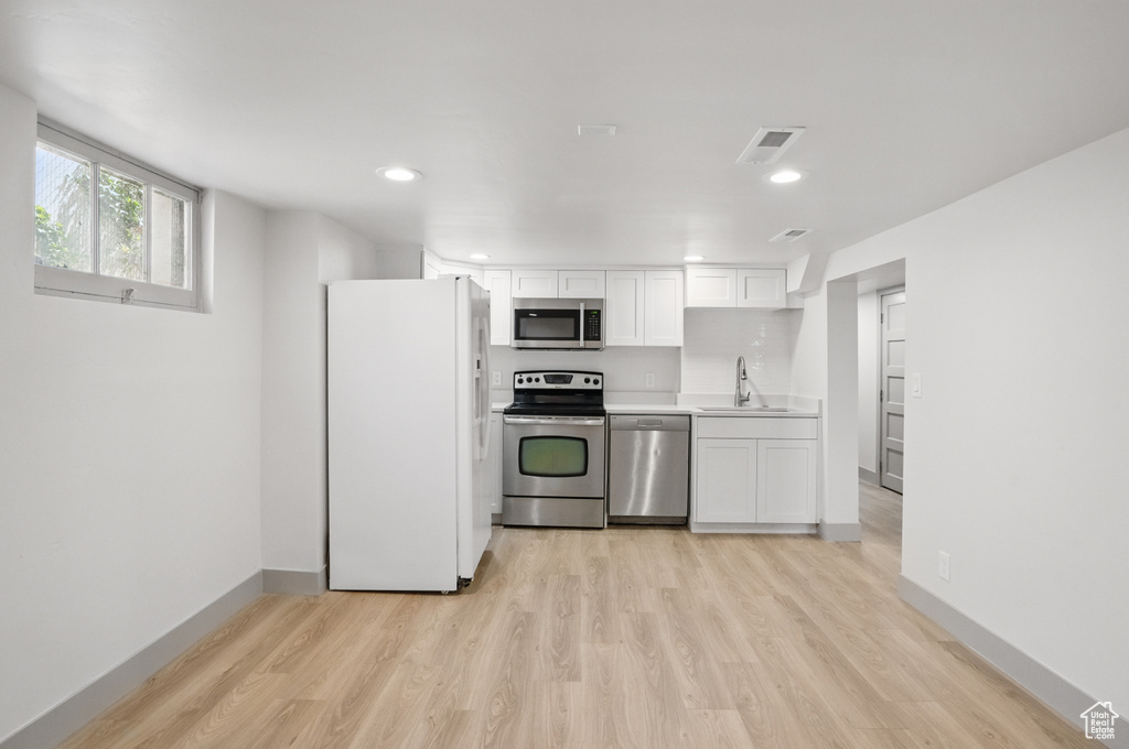 Kitchen featuring stainless steel appliances, a sink, light wood-style flooring, white cabinets, and light countertops