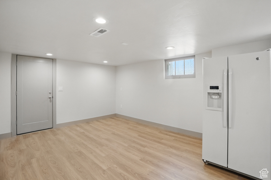 Basement with white refrigerator with ice dispenser, light wood finished floors, and recessed lighting