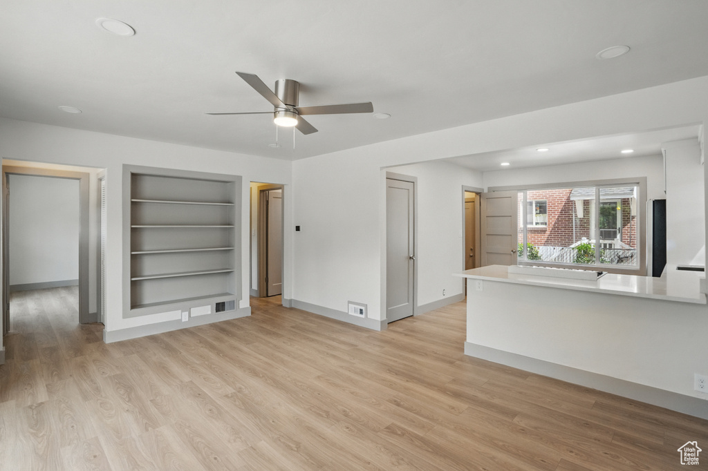 Unfurnished living room featuring built in shelves, a ceiling fan, light wood finished floors, recessed lighting, and baseboards