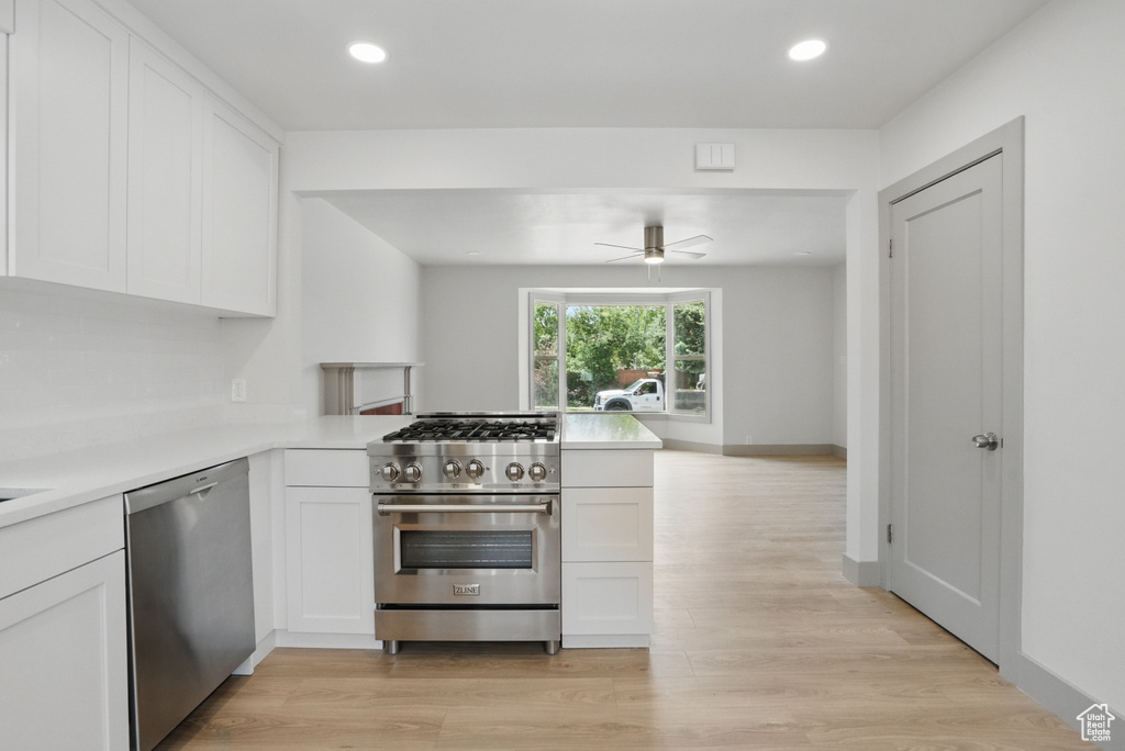 Kitchen featuring appliances with stainless steel finishes, a peninsula, light countertops, white cabinetry, and light wood-type flooring