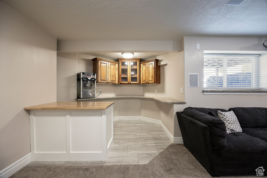 Kitchen featuring brown cabinets, wooden counters, a textured ceiling, glass insert cabinets, and a peninsula