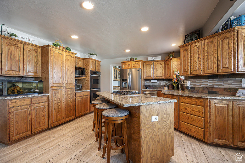 Kitchen with stainless steel appliances, a kitchen island, tasteful backsplash, brown cabinets, and recessed lighting
