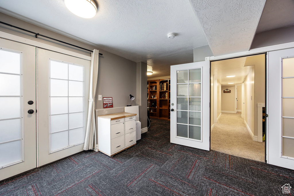 Entryway with french doors, dark carpet, and a textured ceiling