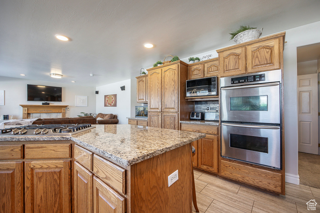 Kitchen with stainless steel appliances, open floor plan, light stone counters, a fireplace, and recessed lighting